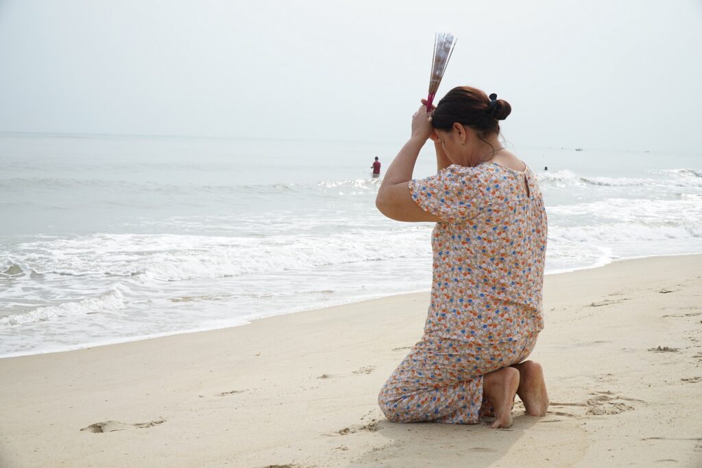 A woman kneels down on the shore praying