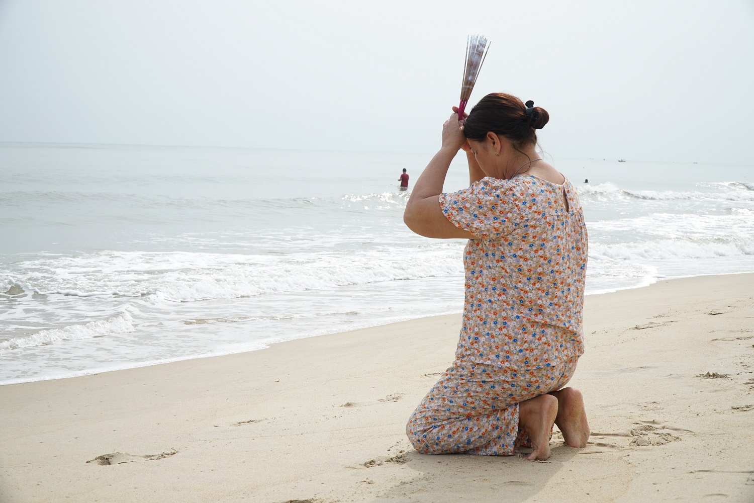 A woman kneels down on the shore praying